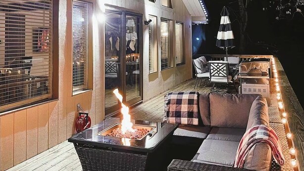 Ein Terrassenbereich im Freien mit Feuerstelle, Korbmöbeln und Lichterketten.
