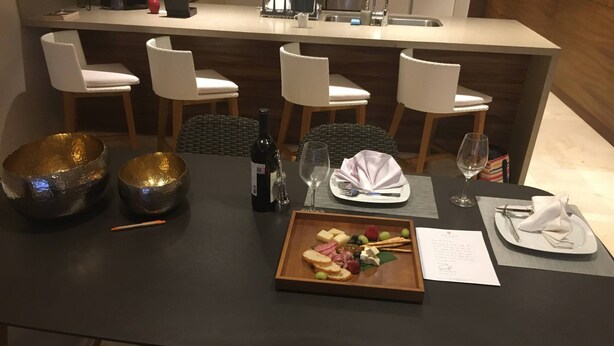 Una mesa de comedor preparada con una tabla de embutidos, una botella de vino, copas y un menú.