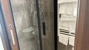 A glass-enclosed shower with a control panel, a towel rack with folded towels, and a wooden door frame. - Urban Stay Siena (Siena)