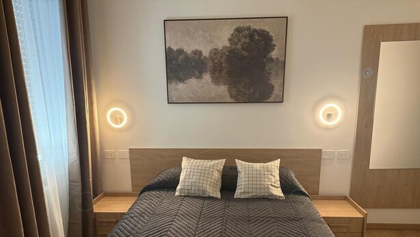 A neatly arranged bedroom with a large bed, two bedside tables, a wall-mounted artwork, and two wall sconces. - Urban Stay Siena (Siena)