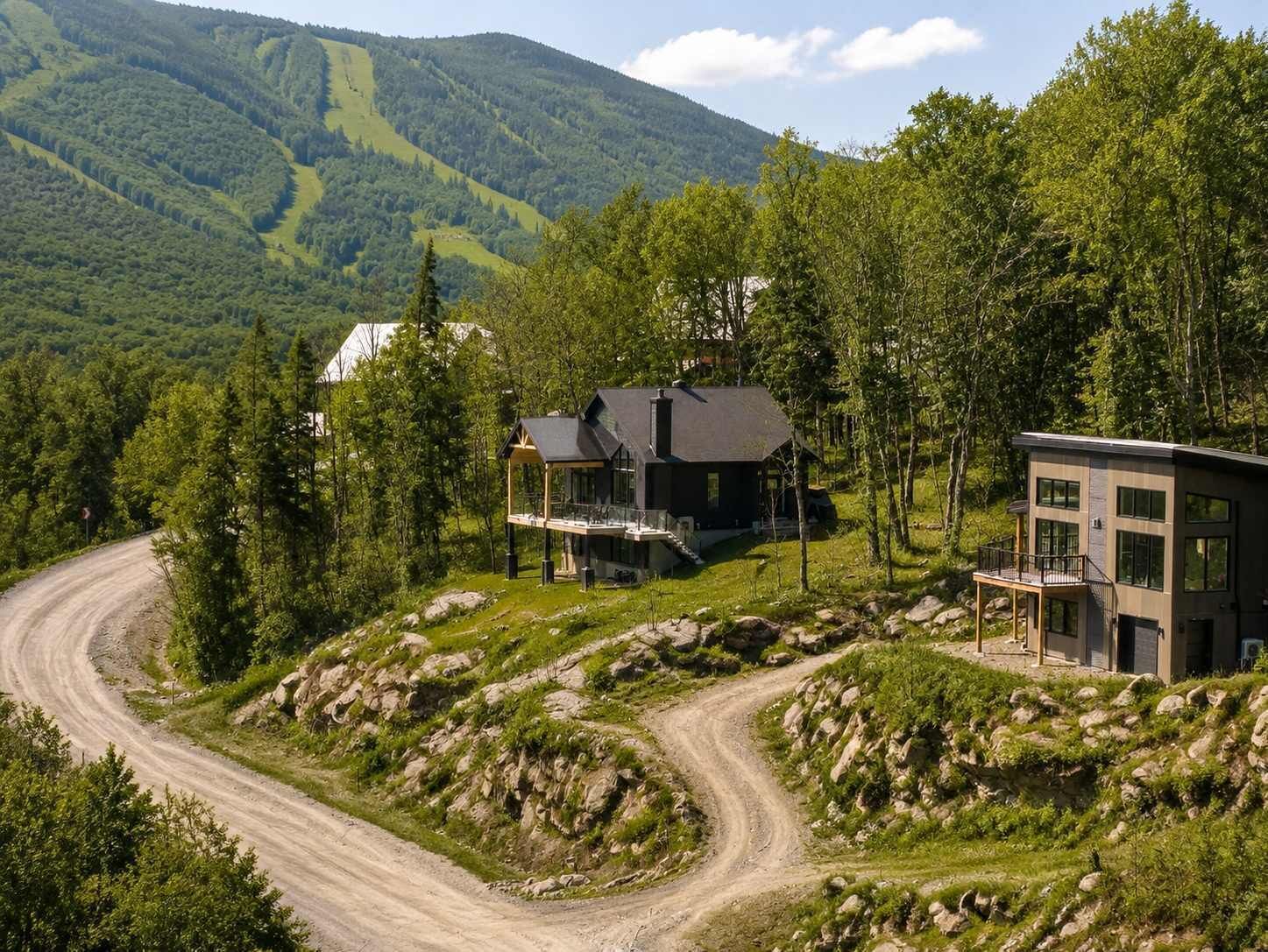 Une maison à deux étages, dotée d’un porche abrité et d’une extension moderne, entourée d’un paysage boisé et bordée d’un chemin de terre sinueux.
