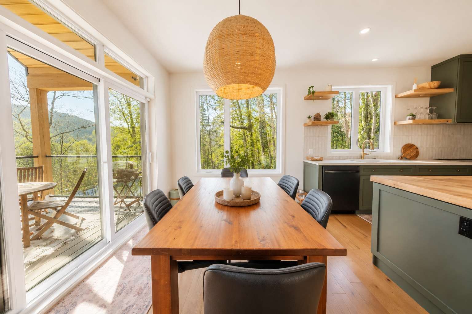 A modern kitchen with a wooden dining table, black chairs, and a hanging light fixture.