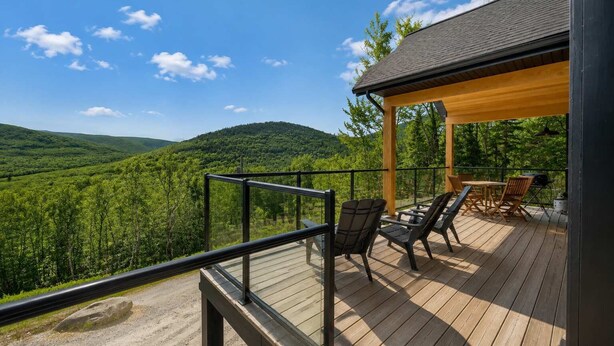 Une terrasse en bois avec des sièges d’extérieur, offrant une vue sur une vallée boisée.