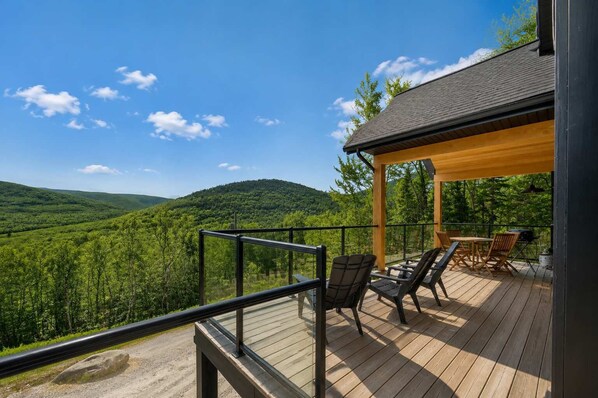 A wooden deck with outdoor seating, overlooking a forested valley.