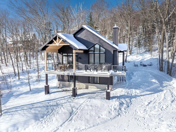 A modern cabin with a covered deck, large windows, and a chimney.