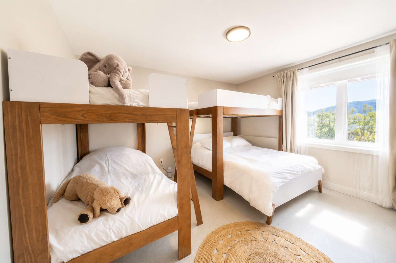 Une chambre avec des lits superposés, une fenêtre donnant sur un beau paysage et un tapis en fibres naturelles sur le sol.