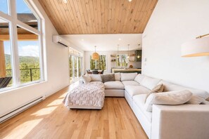 Un salón amplio con un sofá modular blanco grande, techo de madera y vistas al exterior a través de ventanas amplias.