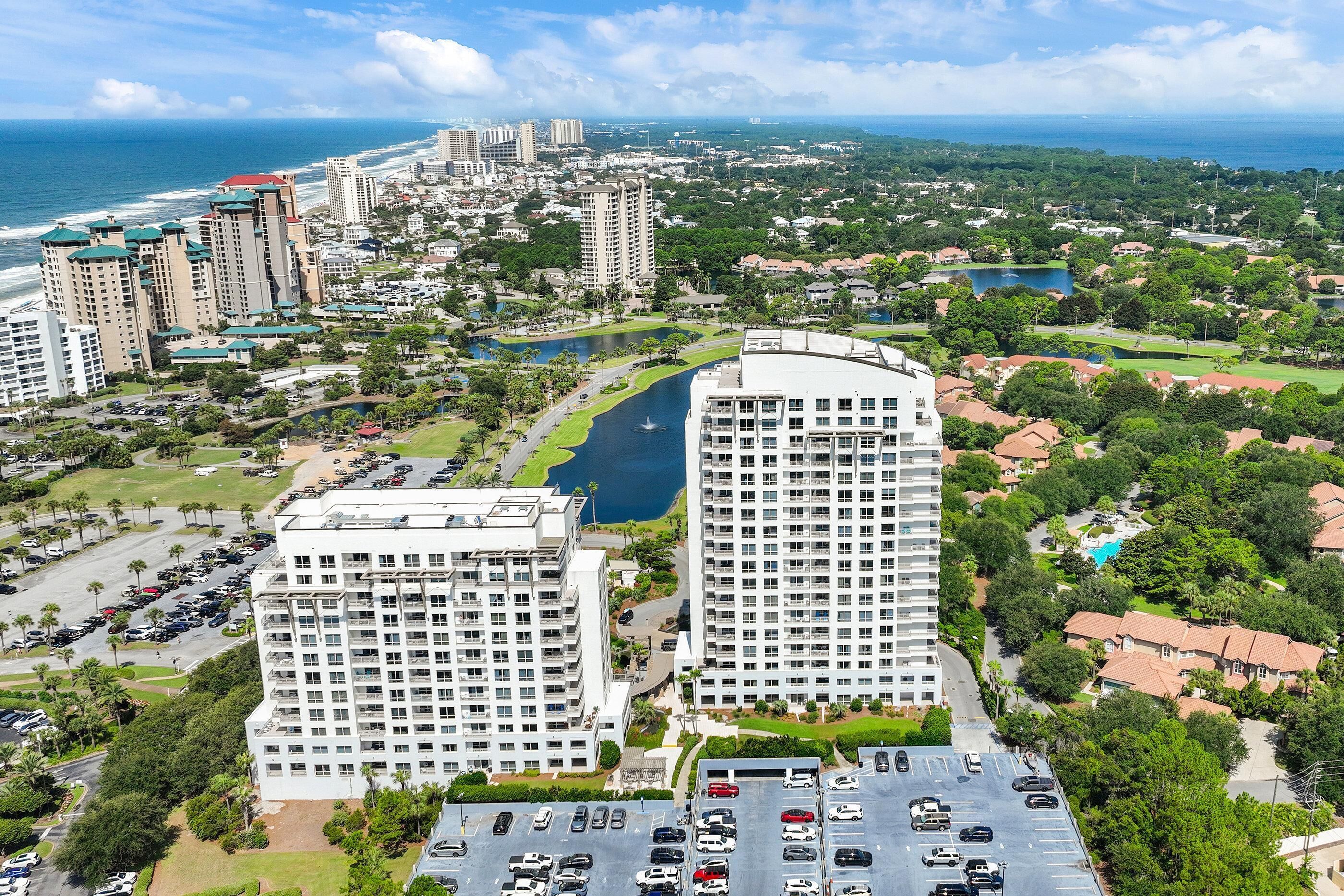 A high-rise hotel with multiple floors, a parking lot, and a view of the ocean.