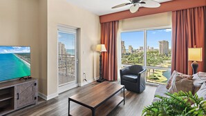 A modern living room with a television, a ceiling fan, a sofa, and a view of a cityscape. - Luau II 6930 (Miramar Beach)