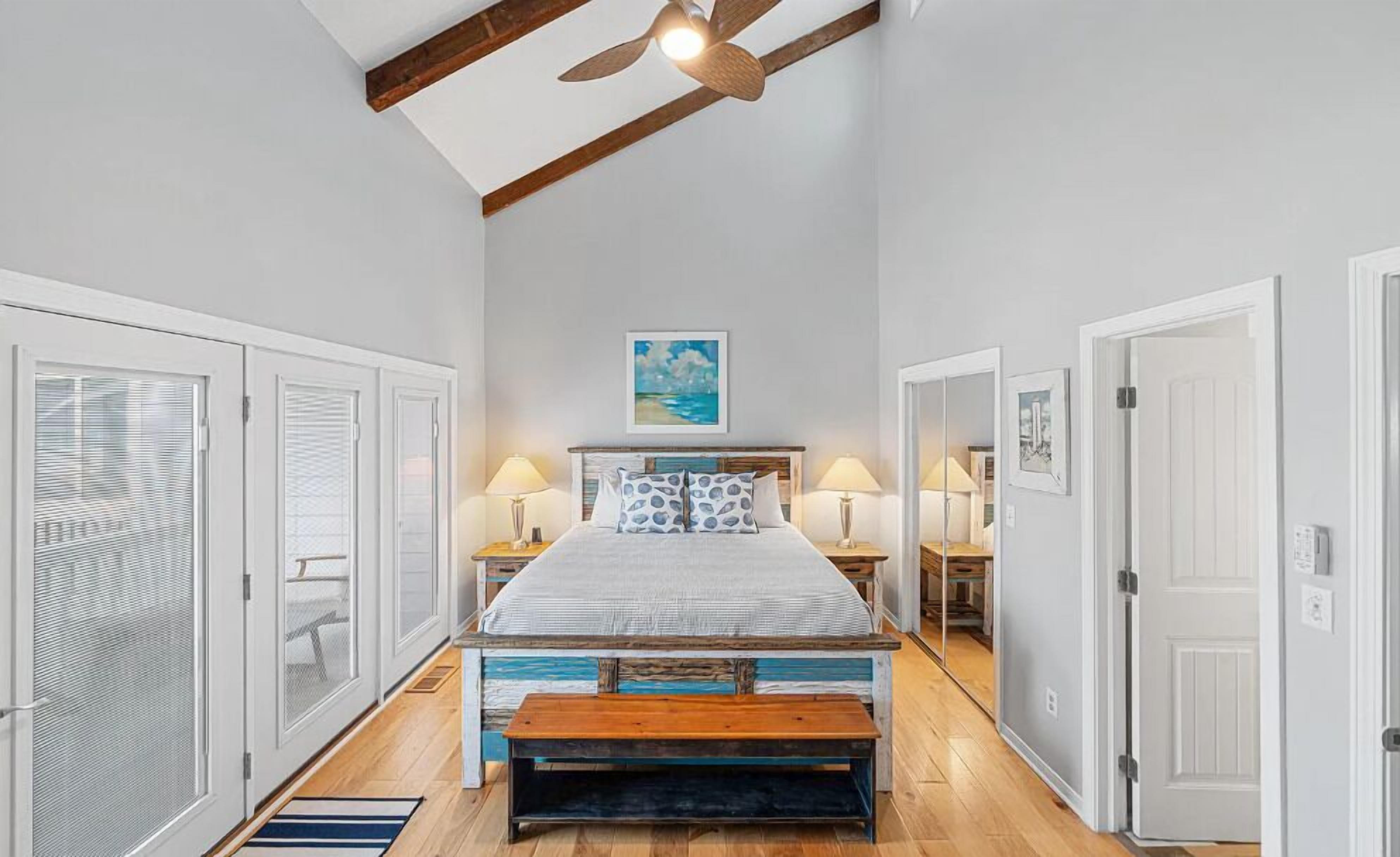 A bedroom with a bed, two bedside lamps, a ceiling fan, and a painting on the wall.