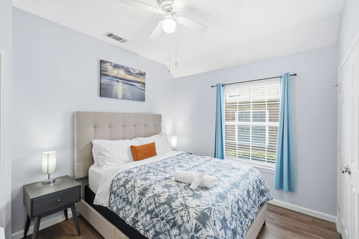 A neatly arranged bedroom with a bed, nightstand, and a window with curtains.