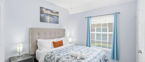 A neatly arranged bedroom with a bed, nightstand, and a window with curtains.