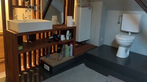 Een badkamer met een houten wastafelmeubel, een wastafel, een spiegel, een toilet en een plank met toiletartikelen.