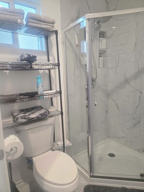 Ein Badezimmer mit Duschkabine, Toilette und Regalen mit Handtüchern und Pflegeprodukten.