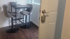 Ein Zimmer mit Esstisch und Stühlen, einer Tür mit Messinggriff und einem Fenster mit Jalousien.