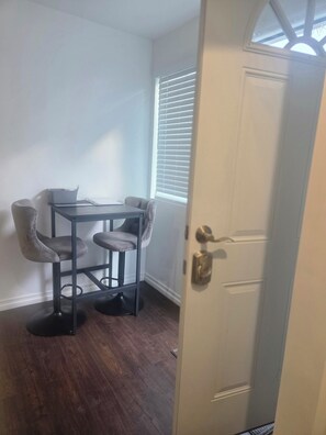 A room with a dining table and chairs, a door with a brass handle, and a window with blinds. - Cozy Local Weekend Escape (Whittier)