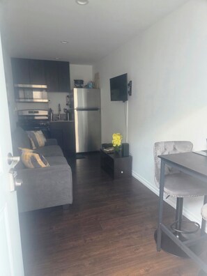 A modern kitchen with a refrigerator, microwave, and stove. There is a gray sofa with decorative pillows and a small table with a vase of flowers. - Cozy Local Weekend Escape (Whittier)
