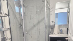 Ein Badezimmer mit einer Duschkabine, einer Toilette, einem Waschbecken mit Spiegel und einem Handtuchhalter.