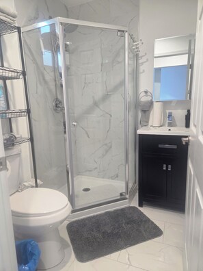 A bathroom with a glass-enclosed shower, a toilet, a sink with a mirror, and a towel rack. - Cozy Local Weekend Escape (Whittier)