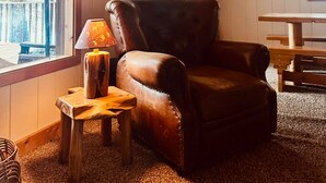 A cozy room with a leather armchair, a wooden table, and a deer head mounted on the wall. - Cozy, Rustic 4-bedroom Lake-view Cabin in the Woods (Cascade)