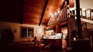 A cozy, dimly lit wooden cabin interior with a high ceiling, a dining area, and a kitchen. - Cozy, Rustic 4-bedroom Lake-view Cabin in the Woods (Cascade)