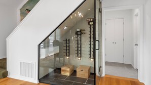 A modern staircase with glass railings, a chandelier, and wine bottles displayed on the wall. - Peaceful Riverfront Retreat with Stunning Views (Mountain Home)