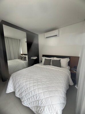 A modern hotel room with a large bed, a bedside table, a mirror, and an air conditioning unit on the wall. - PORTO 2 LIFE GAV- MARÉ ALTA (Ipojuca)