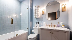 A bathroom with a glass shower enclosure, a white toilet, a vanity with a marble countertop, and a wall-mounted mirror. - Hollyhock Suite 406: 1 bed/1 bath (Louisville)