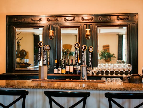 Zona de bar con varias llaves de cerveza etiquetadas 'HINTERLAND', una selección de botellas y vasos sobre la barra.