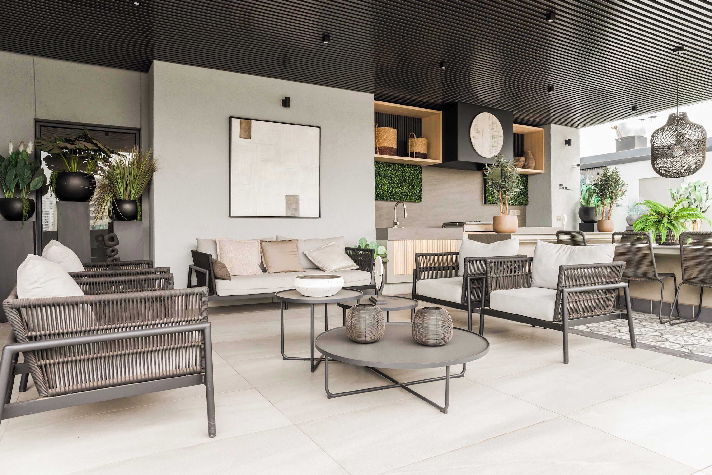 Shared outdoor lounge with woven seating, a landscaped greenery wall, and a convenient kitchenette for relaxing and socializing.