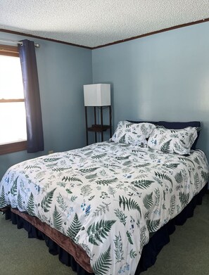 A bedroom with a bed, a nightstand, a lamp, and a window with curtains.