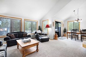 A spacious living room with a black leather sofa, a wooden coffee table, and a dining area with a wooden table and chairs. - Sunriver's Klamath Lane - Hot Tub & SHARC Passes (Sunriver)