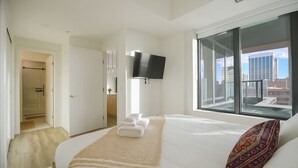 Camera d'albergo con letto, televisione, balcone vista città e zona doccia.