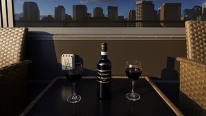 Un balcone con sedie in vimini, un tavolo, una bottiglia di vino Folinar e due bicchieri da vino.