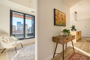 Ein modernes Wohnzimmer mit einem großen Fenster, einem Sofa, einem Holztisch und einem Gemälde an der Wand.