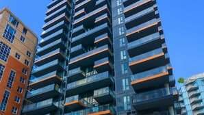 Un edificio a più piani con balconi, circondato da vegetazione e altri edifici.