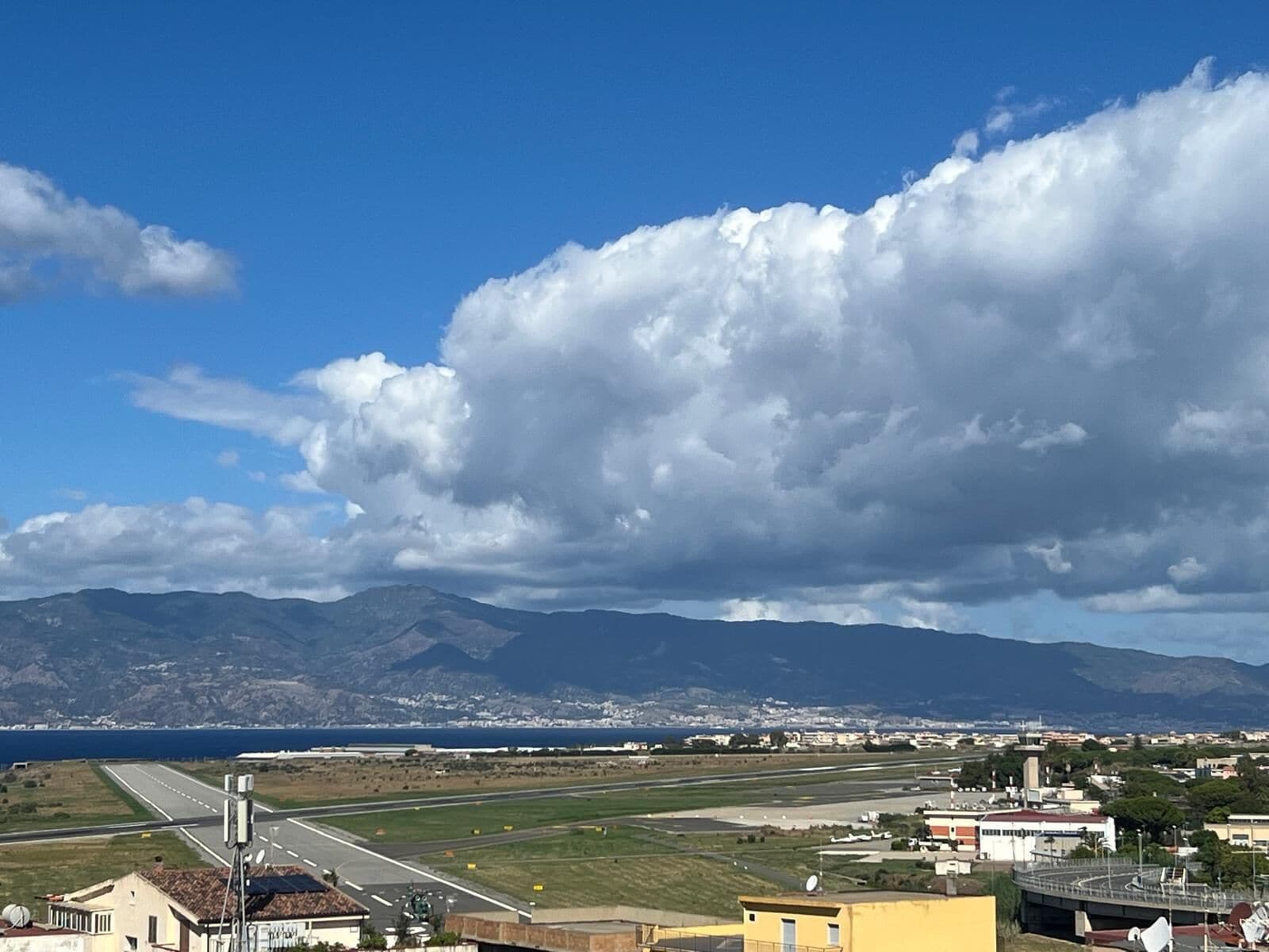 Vista de una zona costera con una pista de aterrizaje, edificios y montañas al fondo.