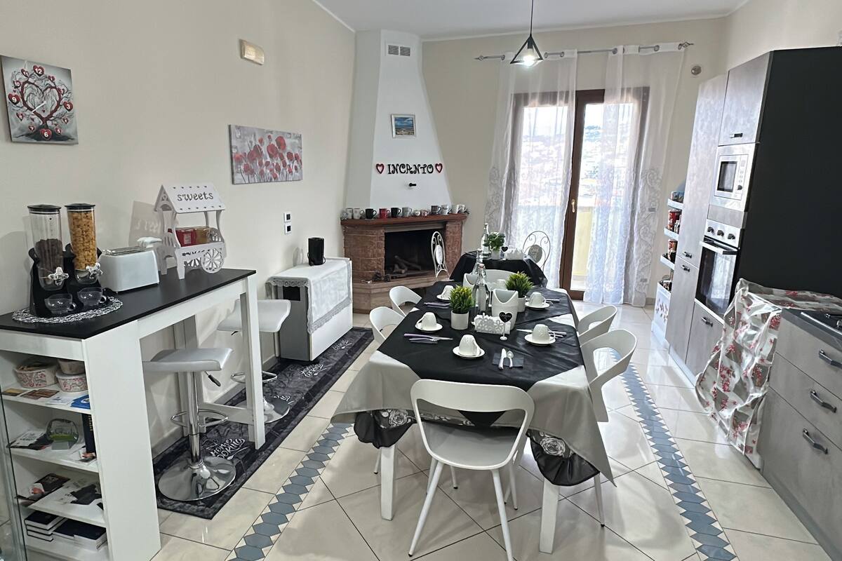 A dining area with a table set for four, a fireplace, and a kitchen with modern appliances.