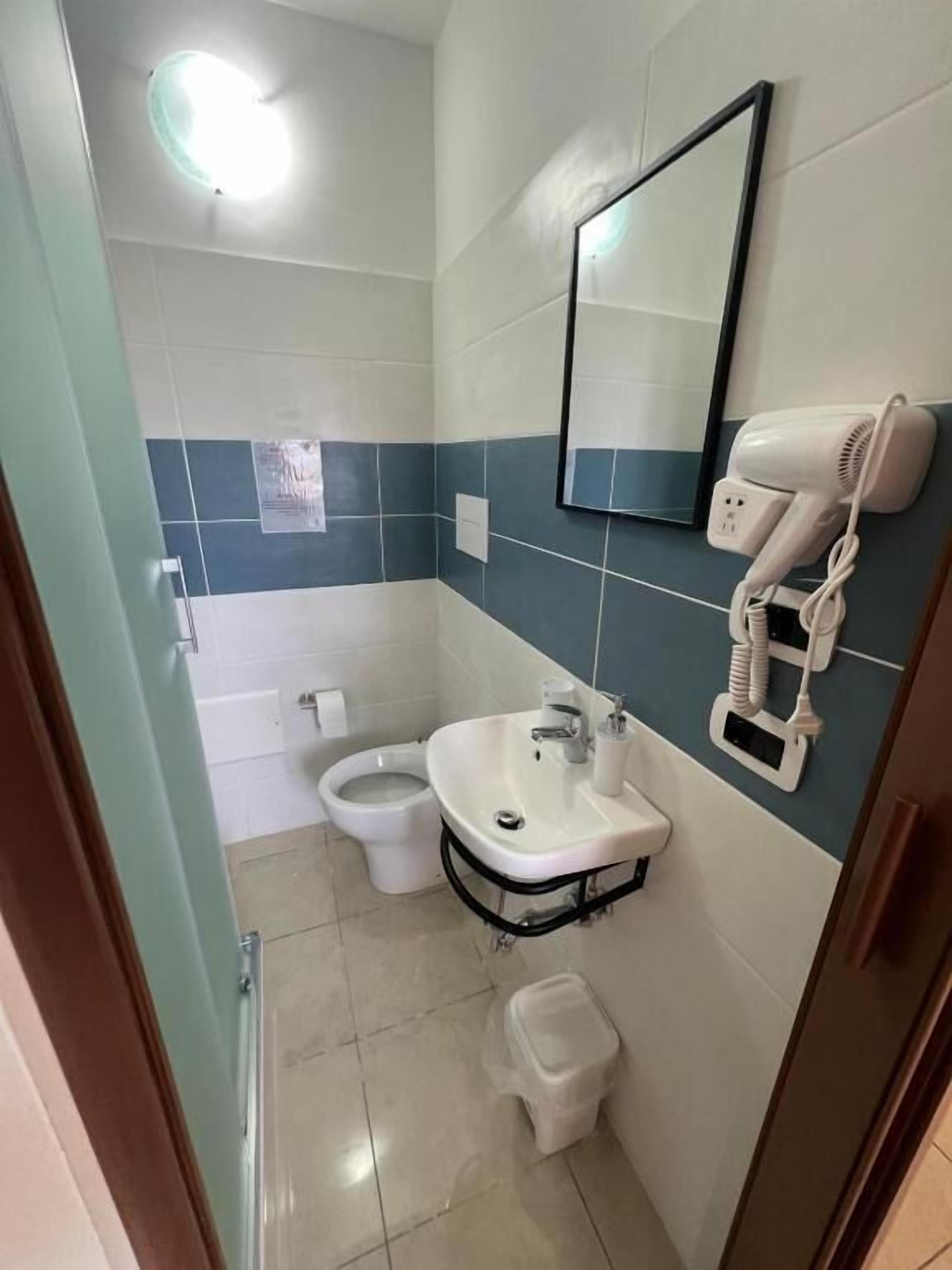 A compact bathroom with a toilet, sink, and hairdryer on a wall-mounted stand.