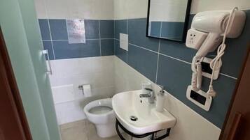 A compact bathroom with a toilet, sink, and hairdryer on a wall-mounted stand.