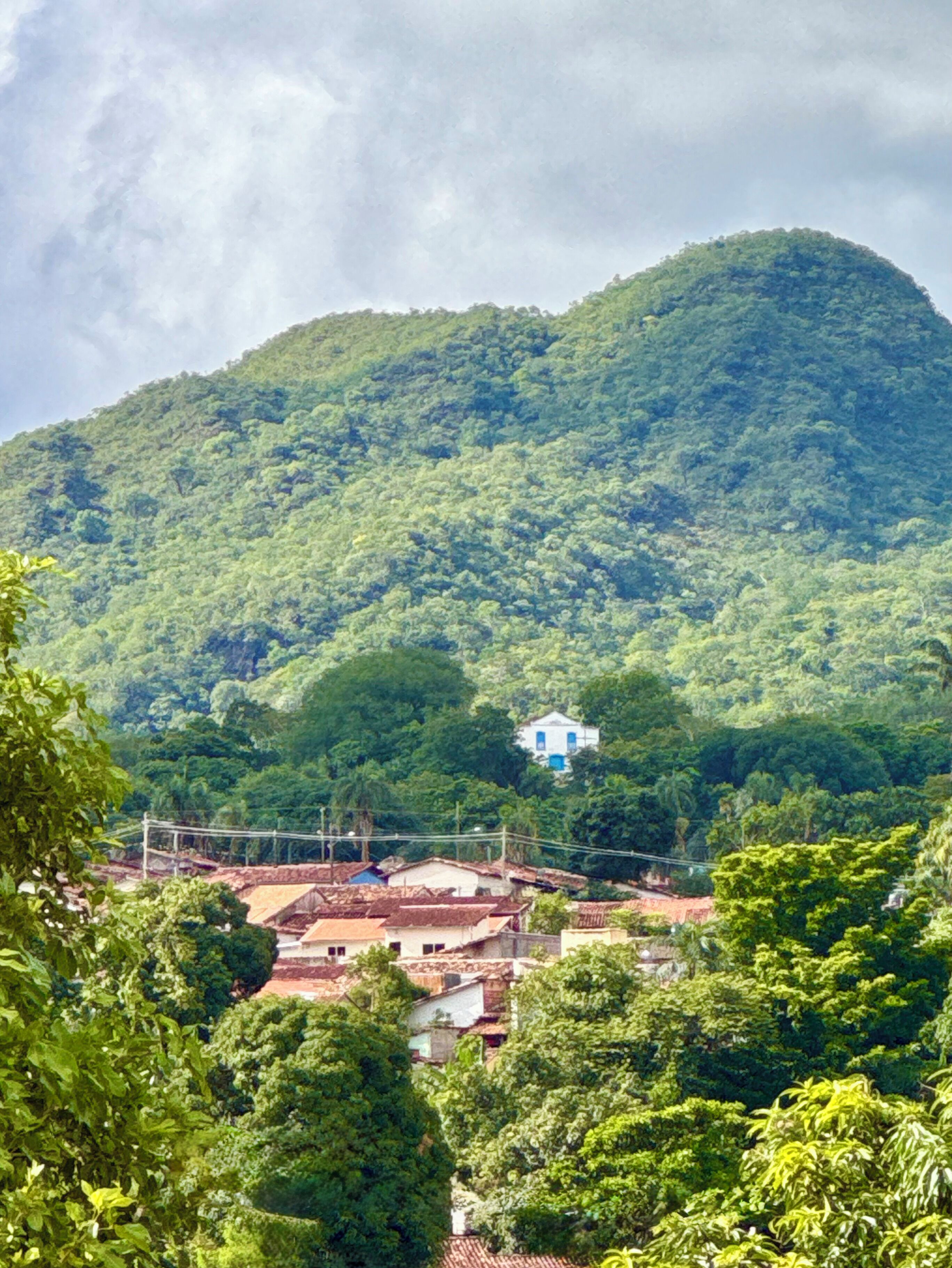 A lush green mountain with a small white building on top.