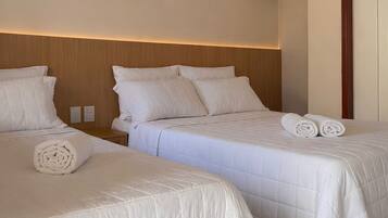 Ein Hotelzimmer mit zwei Betten, jeweils mit weißer Bettwäsche und Kissen. Über den Betten hängt ein gerahmtes Bild, eine Garderobe und eine Tür ist rechts zu sehen.