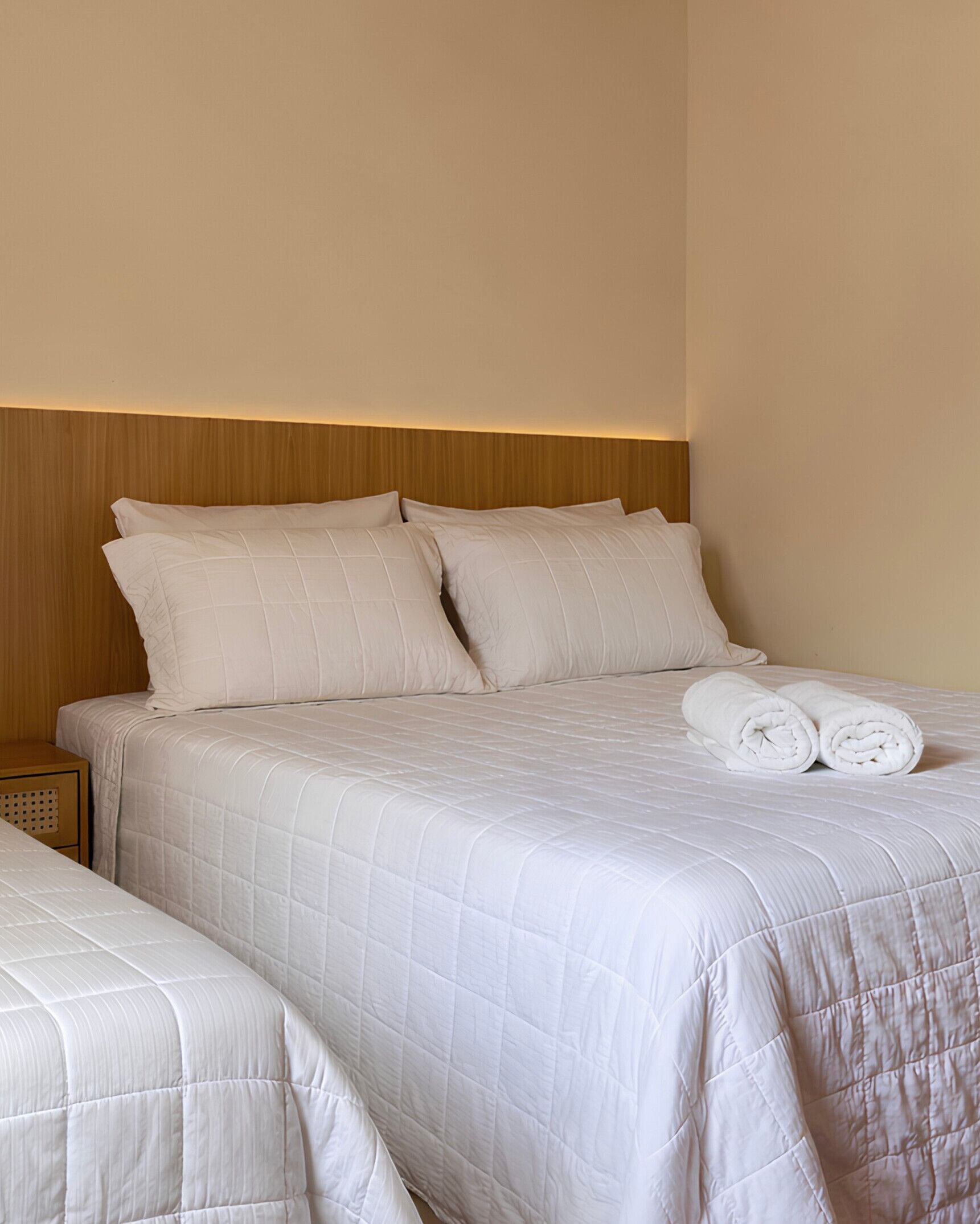 A double bed with a quilted white duvet, two pillows, and a rolled towel on the bed.
