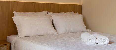 A double bed with a quilted white duvet, two pillows, and a rolled towel on the bed.