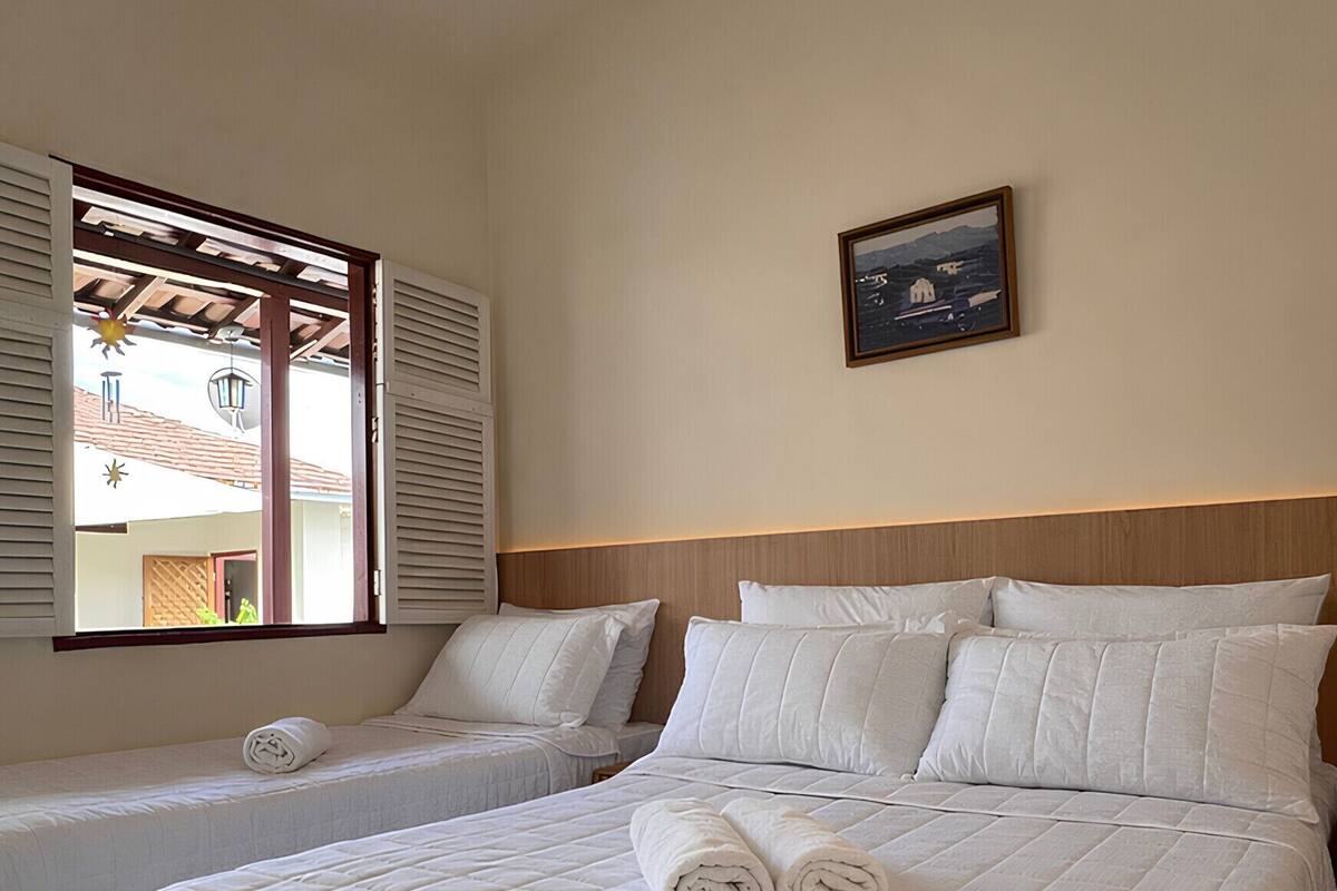 A hotel room with two beds, a large window with shutters, a framed picture on the wall, and a tiled floor.