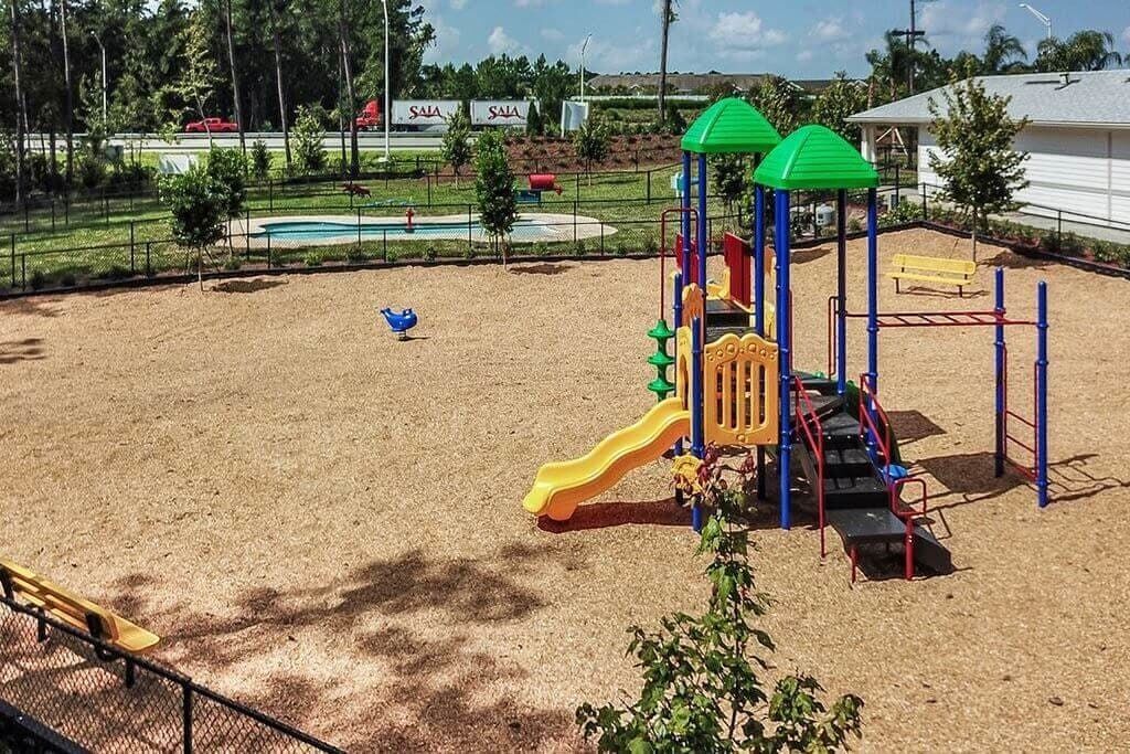 A playground with a yellow slide and climbing structures, surrounded by a fence and trees.