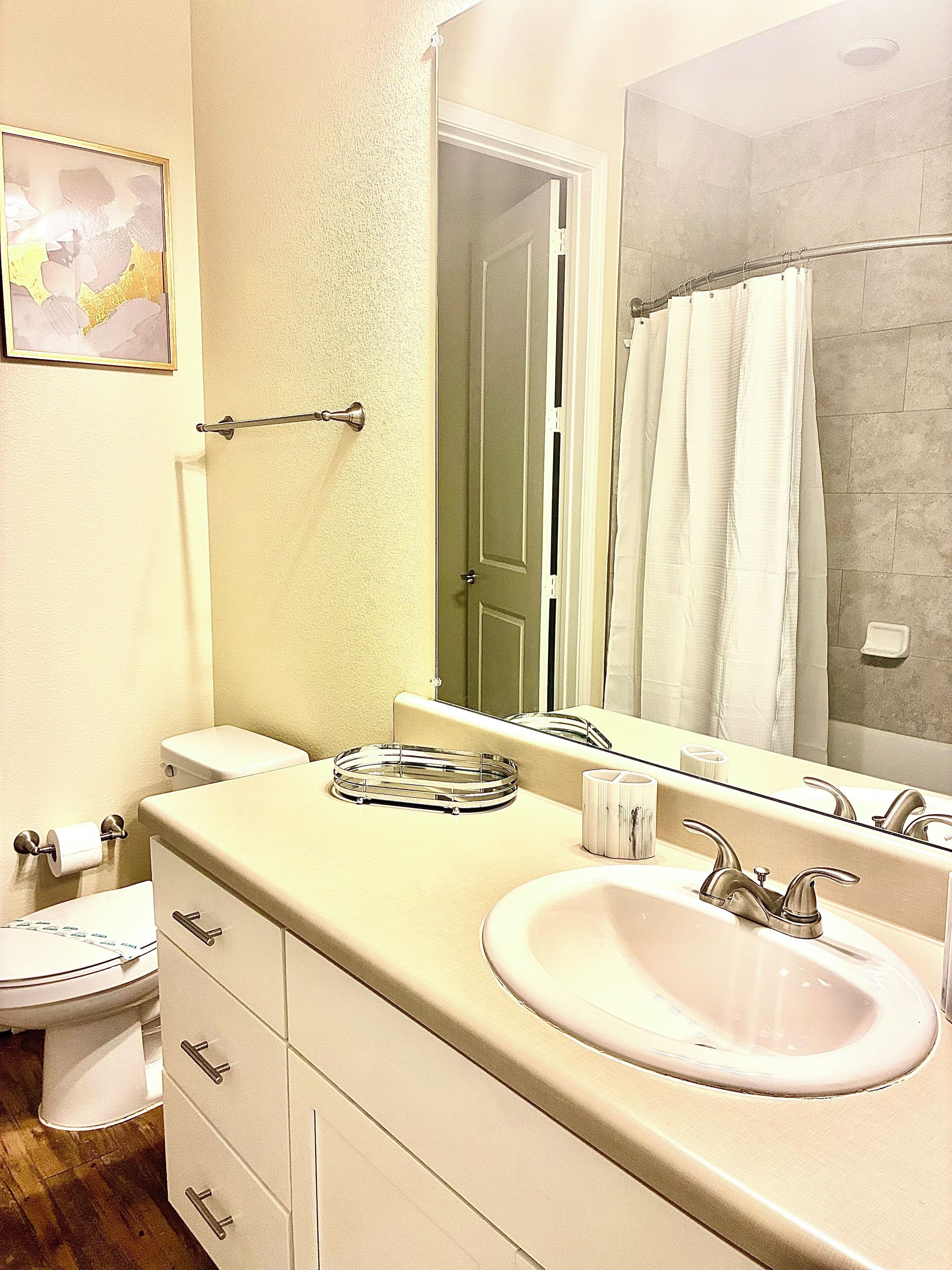 A bathroom with a white sink, a mirror, a toilet, and a shower curtain.