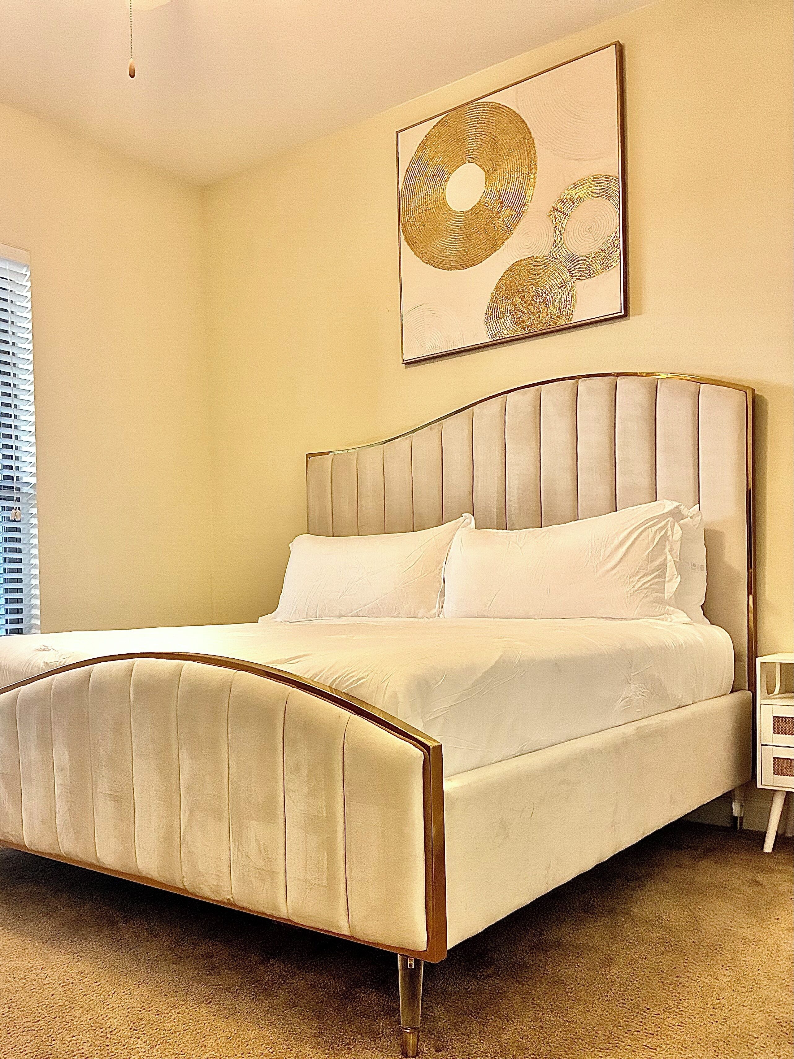 A bedroom with a large bed, a headboard, and a wall-mounted artwork.
