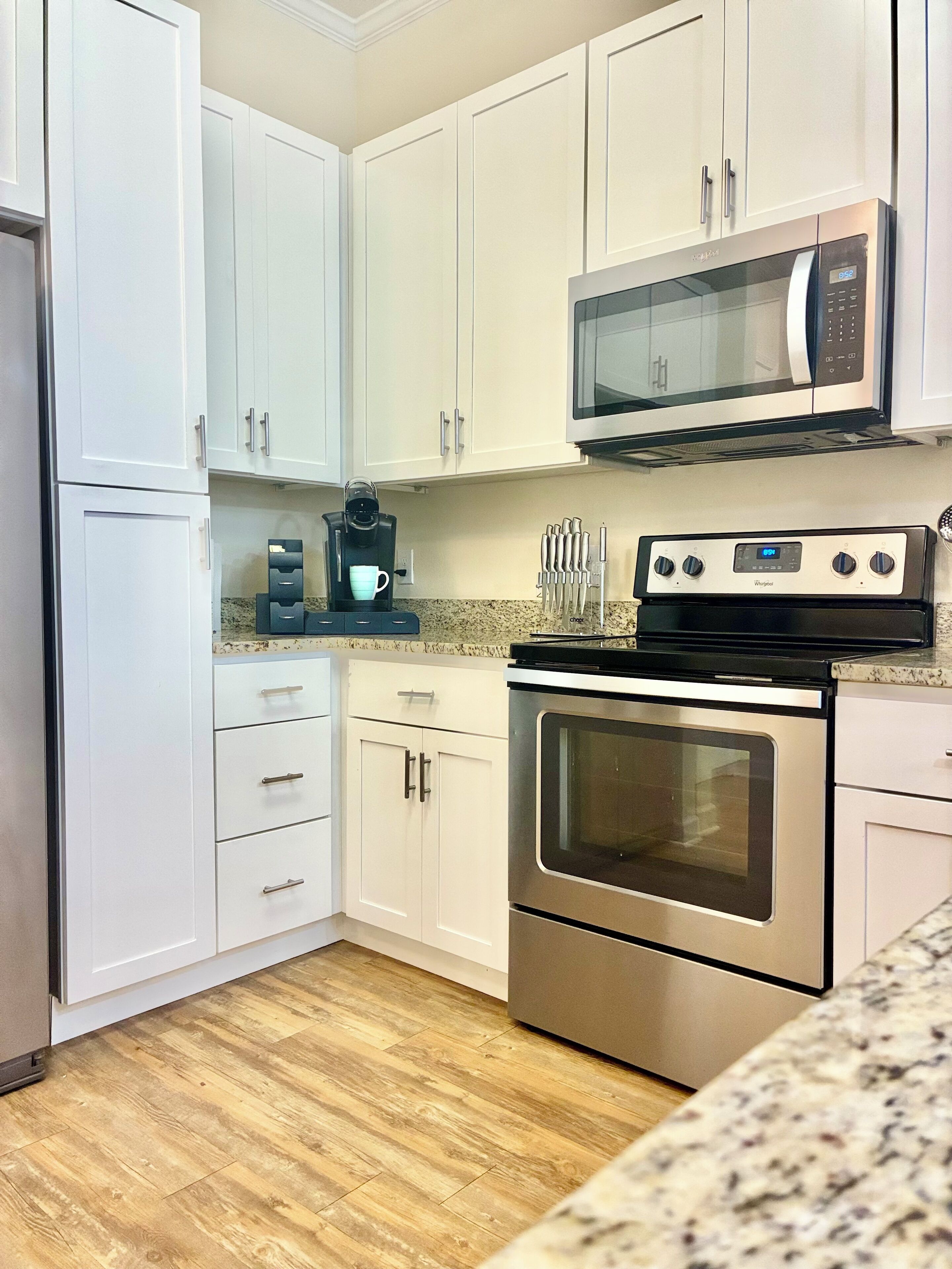 A modern kitchen with white cabinets, a stainless steel oven, a microwave, and a coffee maker.