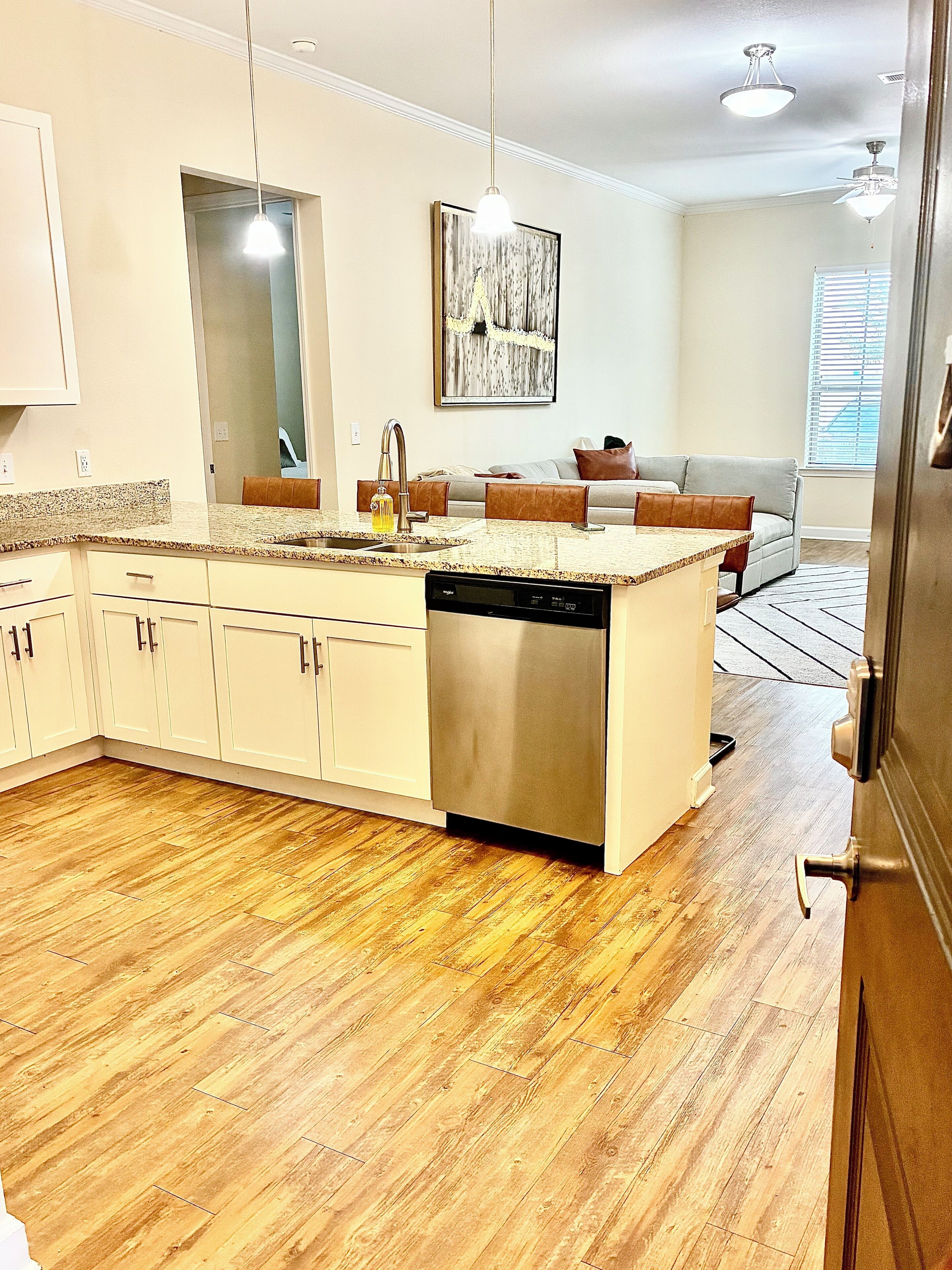A modern kitchen with a central island, stainless steel dishwasher, and a dining area with a sofa and cushions.